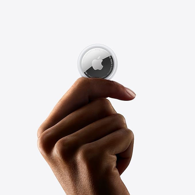 Person holding a single Apple AirTag between fingers, showing its small and portable size.