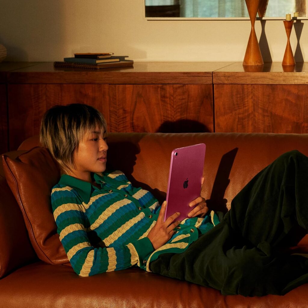 Person relaxing on couch using Apple iPad for reading and entertainment.